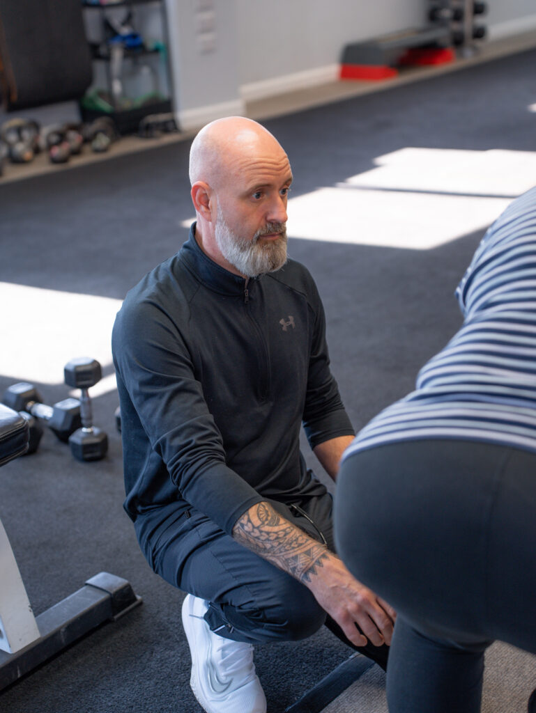 A personal trainer helping a client stay active with back pain in Bedford using a glute bridge exercise.