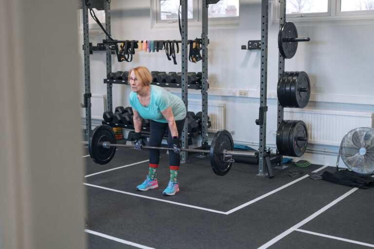 Diane performing a deadlift during a small group personal training session at The Training Gyms in Bedford, focused and confident in front of a weight rack.