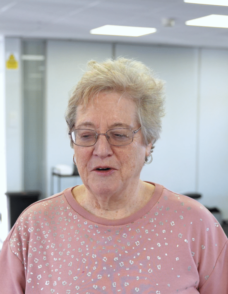 Debbie smiling in a relaxed setting at The Training Gyms in St Albans, wearing a pink jumper with silver patterns, feeling supported and confident.