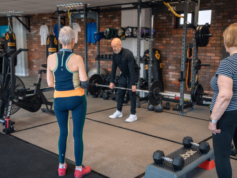 Personal trainer in Hitchin coaching two women on barbell technique in a supportive gym environment.