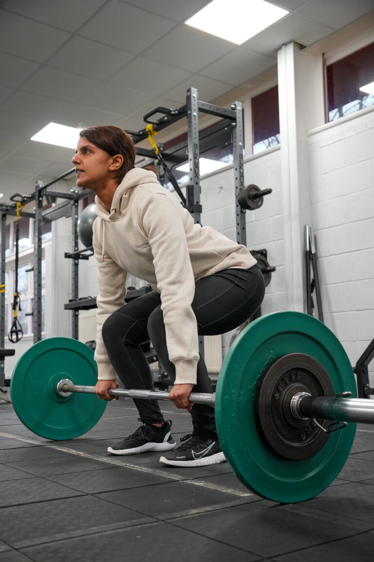 Woman in a hoodie performing a deadlift with green bumper plates at The Training Gyms in Bedford, focused and in proper form during a strength session.