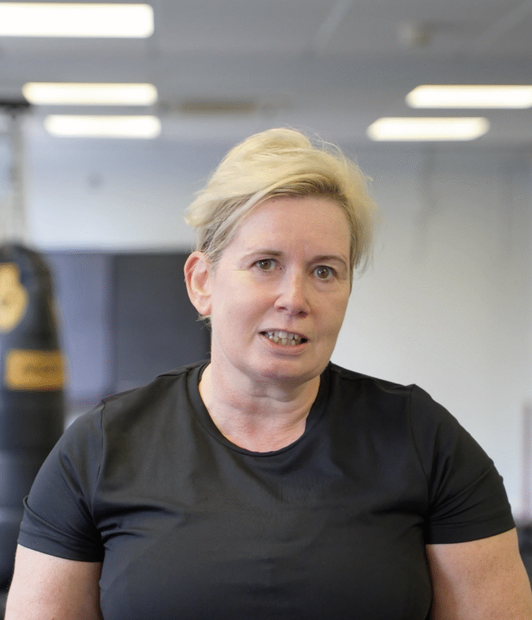 Allison speaking at The Training Gyms in St Albans, wearing gym clothes and standing in front of punch bags, mid-interview about her fitness journey.